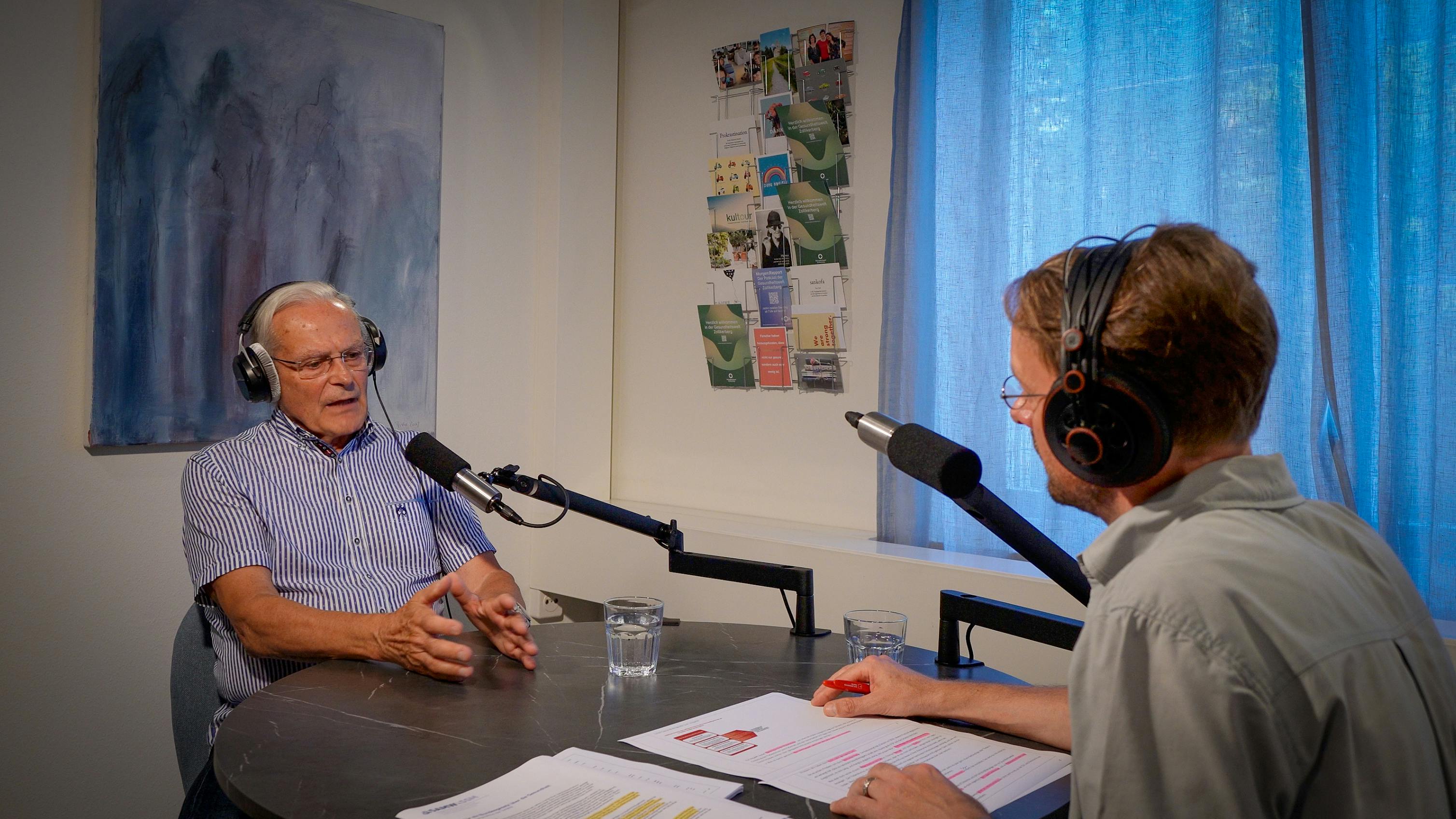 Zwei Personen im Radiostudio beim Interview, eine spricht ins Mikrofon, die andere hört zu.