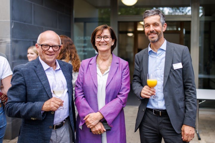 Drei lächelnde Geschäftsleute mit Getränken bei einem Networking-Event.