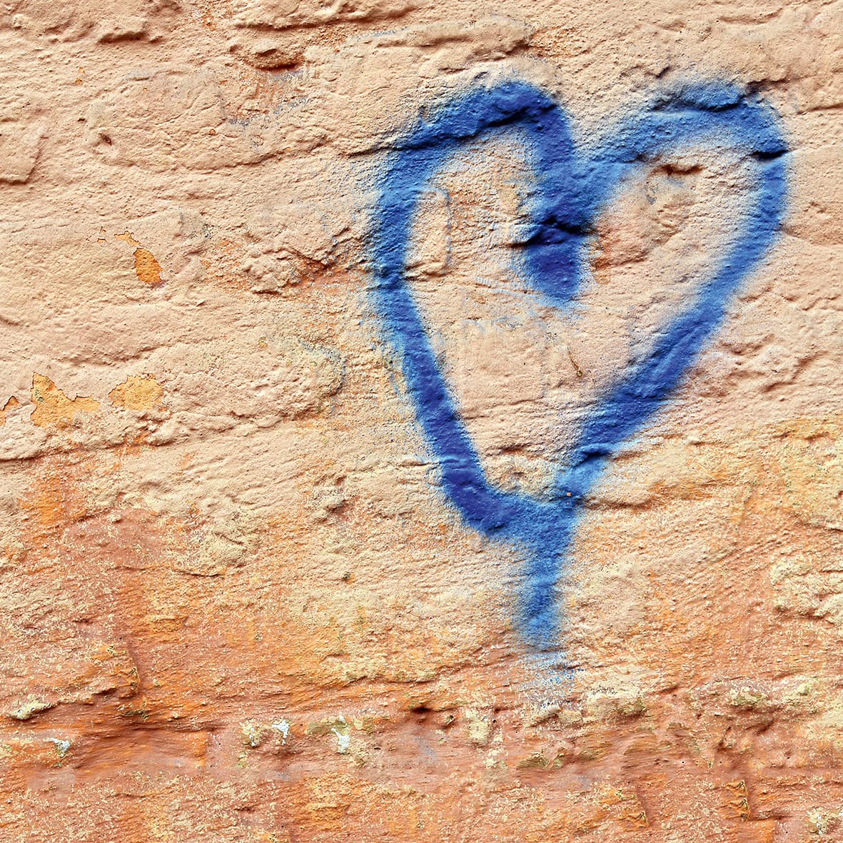 Graffiti-Herz in Blau auf rauer, beiger Wand.