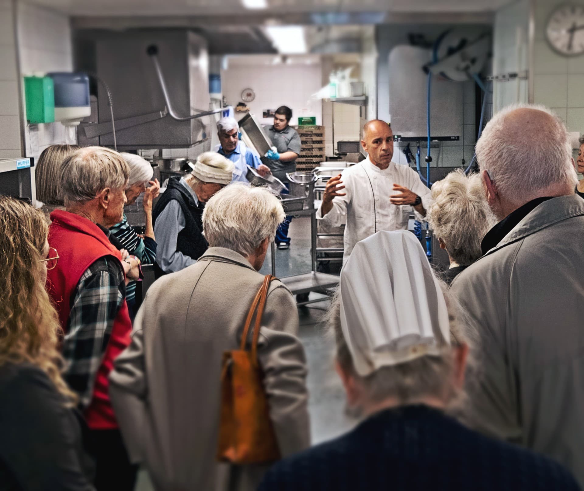 Gruppe bei Küchenführung, Koch erklärt Vorgänge.