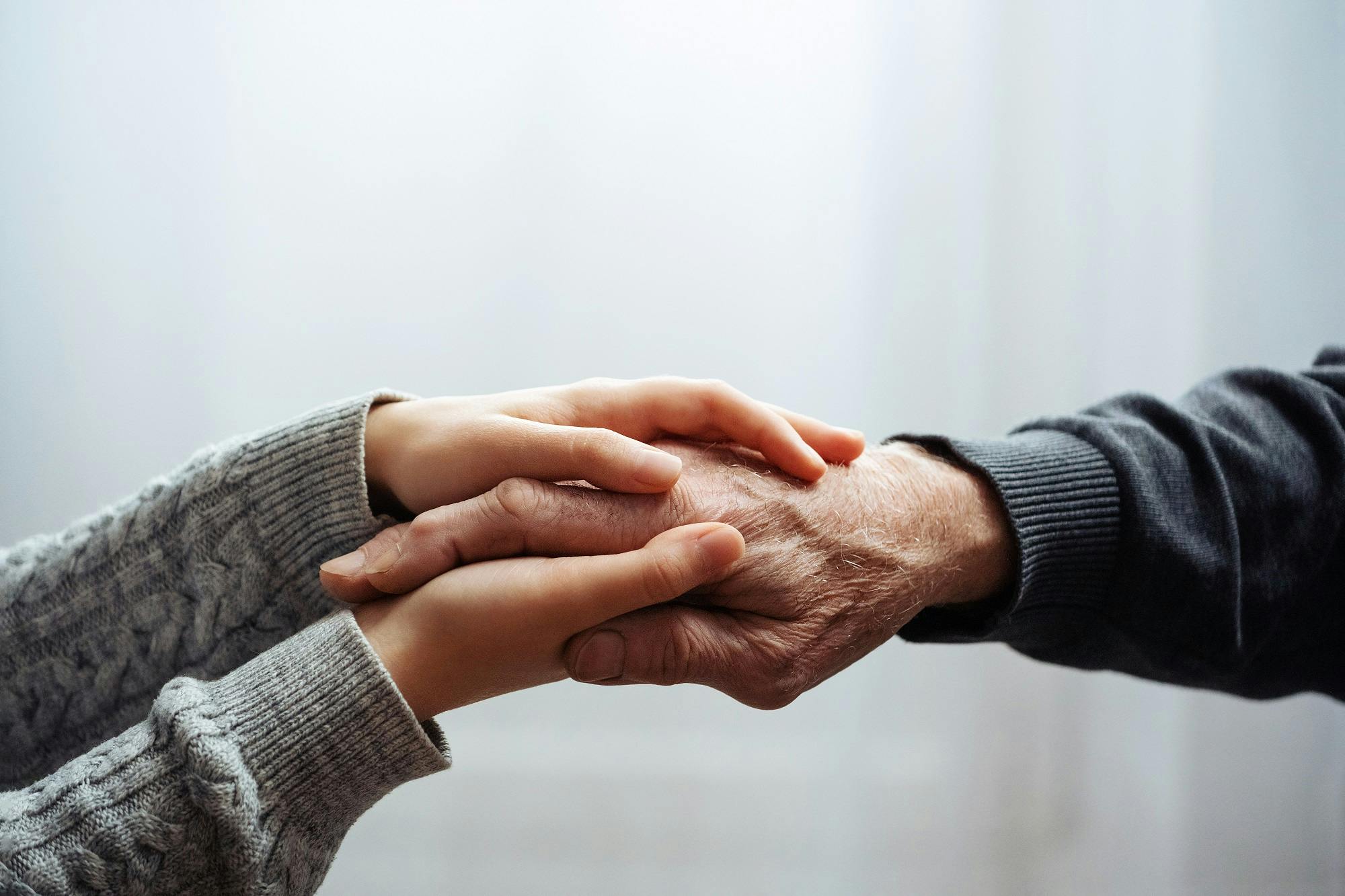 Zwei Personen halten Hände als Zeichen von Fürsorge und Verbundenheit.