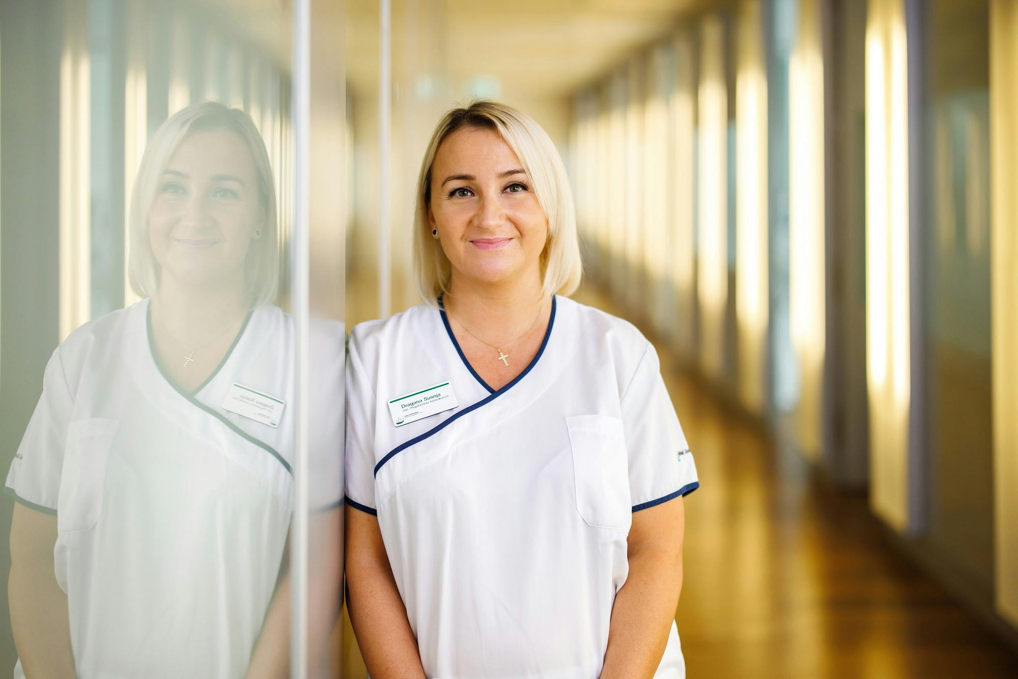 Lächelnde Krankenschwester in weißer Uniform steht im Krankenhausflur.