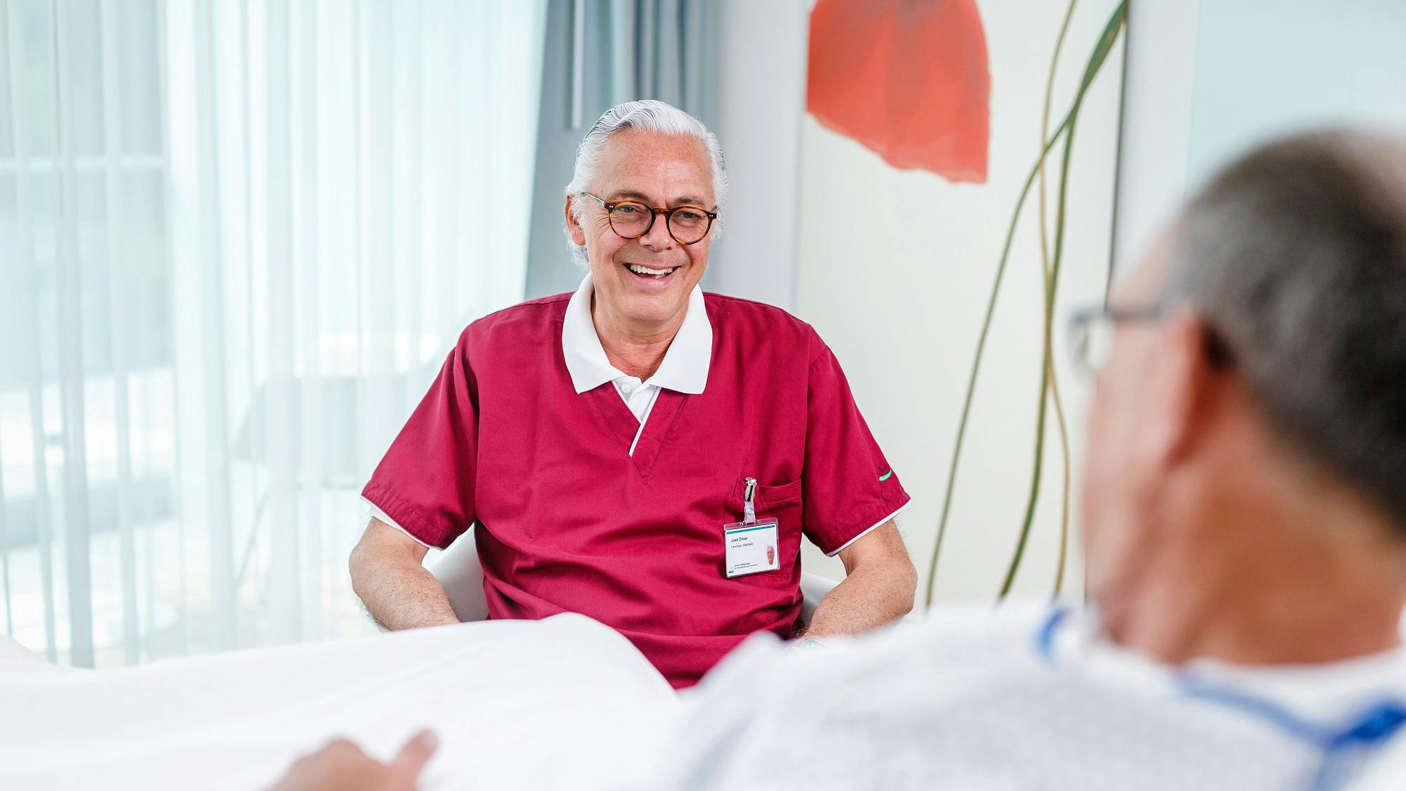 Lächelnder älterer Krankenpfleger im Gespräch mit Patienten im Krankenhauszimmer.