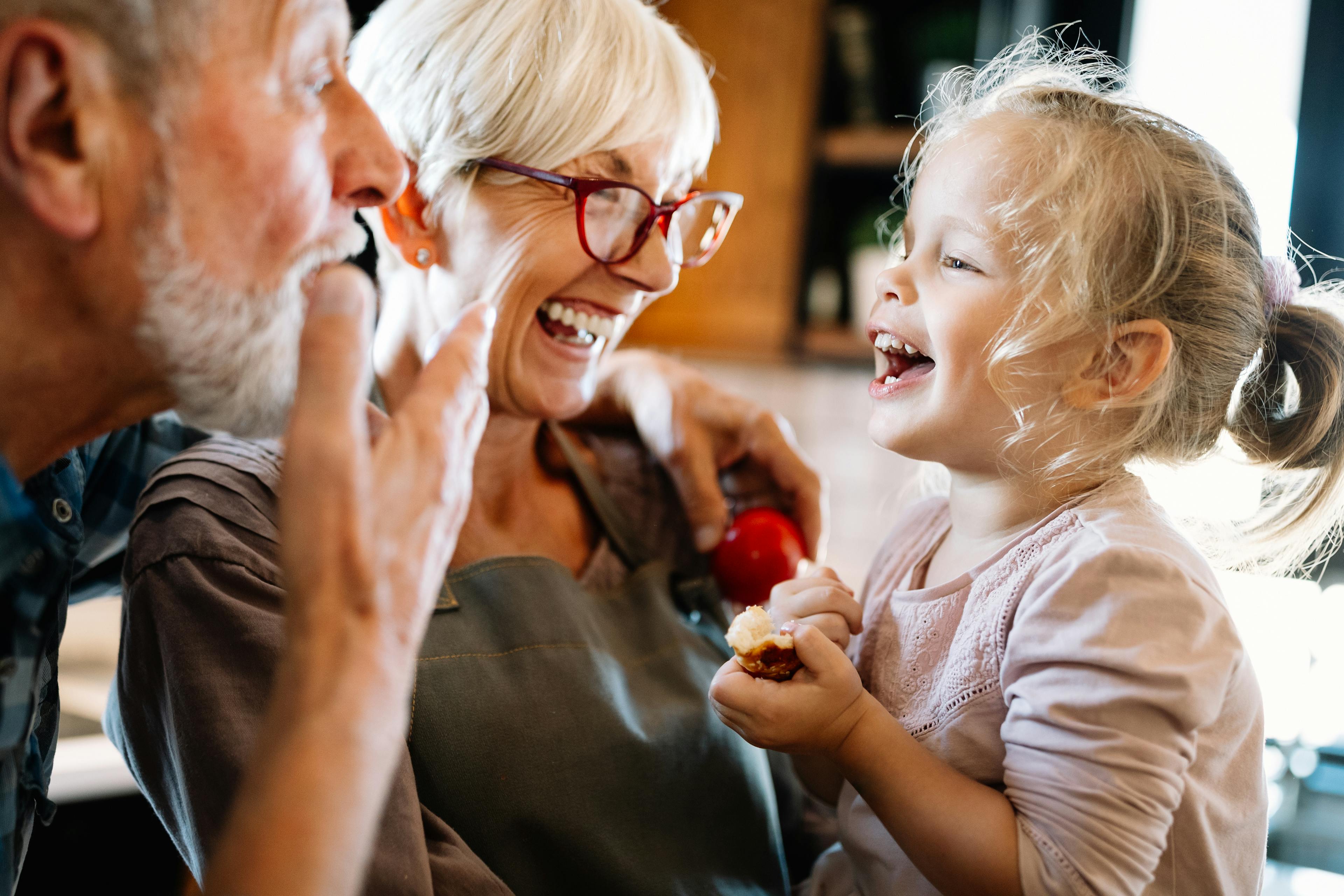 Fröhliche Großeltern lachen mit Enkelin in der Küche.