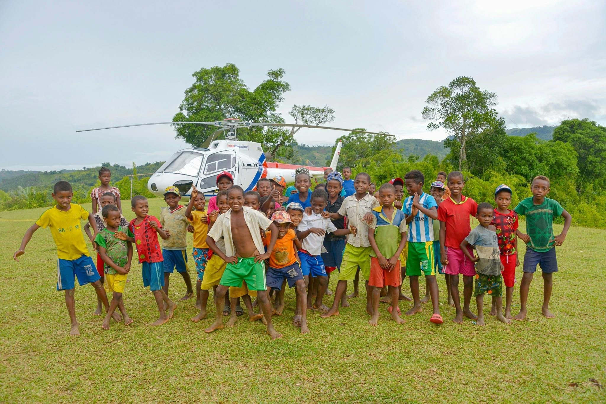 Gruppe lächelnder Kinder vor einem Hubschrauber im ländlichen Gebiet.