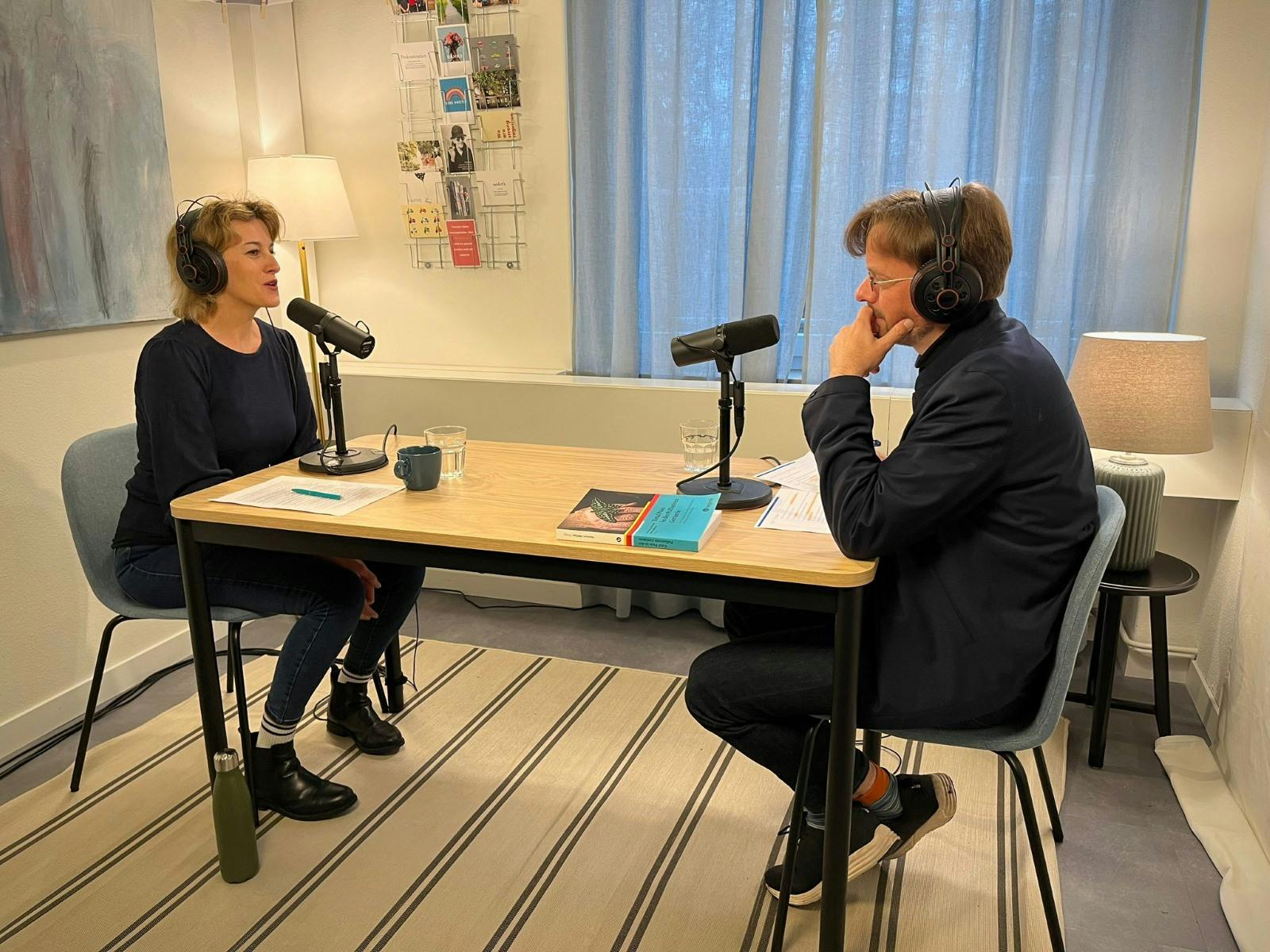 Zwei Personen führen ein Gespräch bei einer Podcast-Aufnahme in einem hellen Raum.
