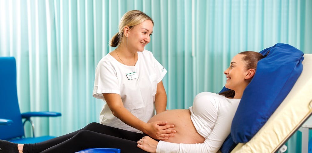 Hebamme betreut lächelnde schwangere Frau.