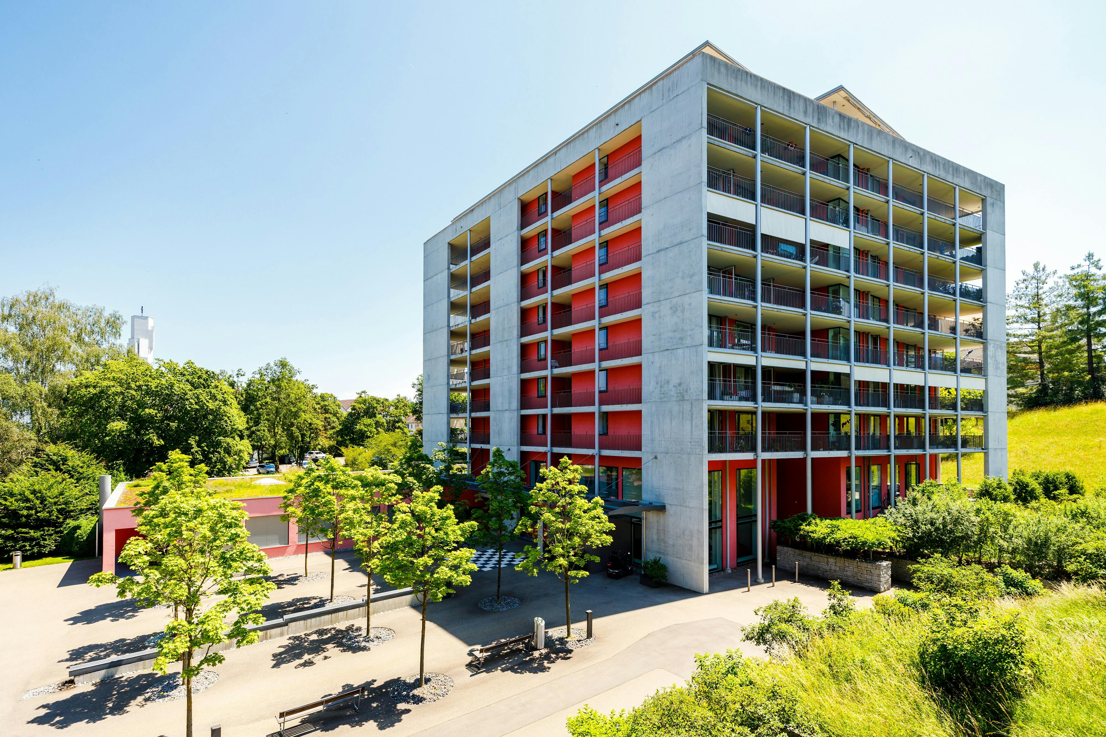 Modernes Wohngebäude mit roten Balkonen und viel Grünfläche.