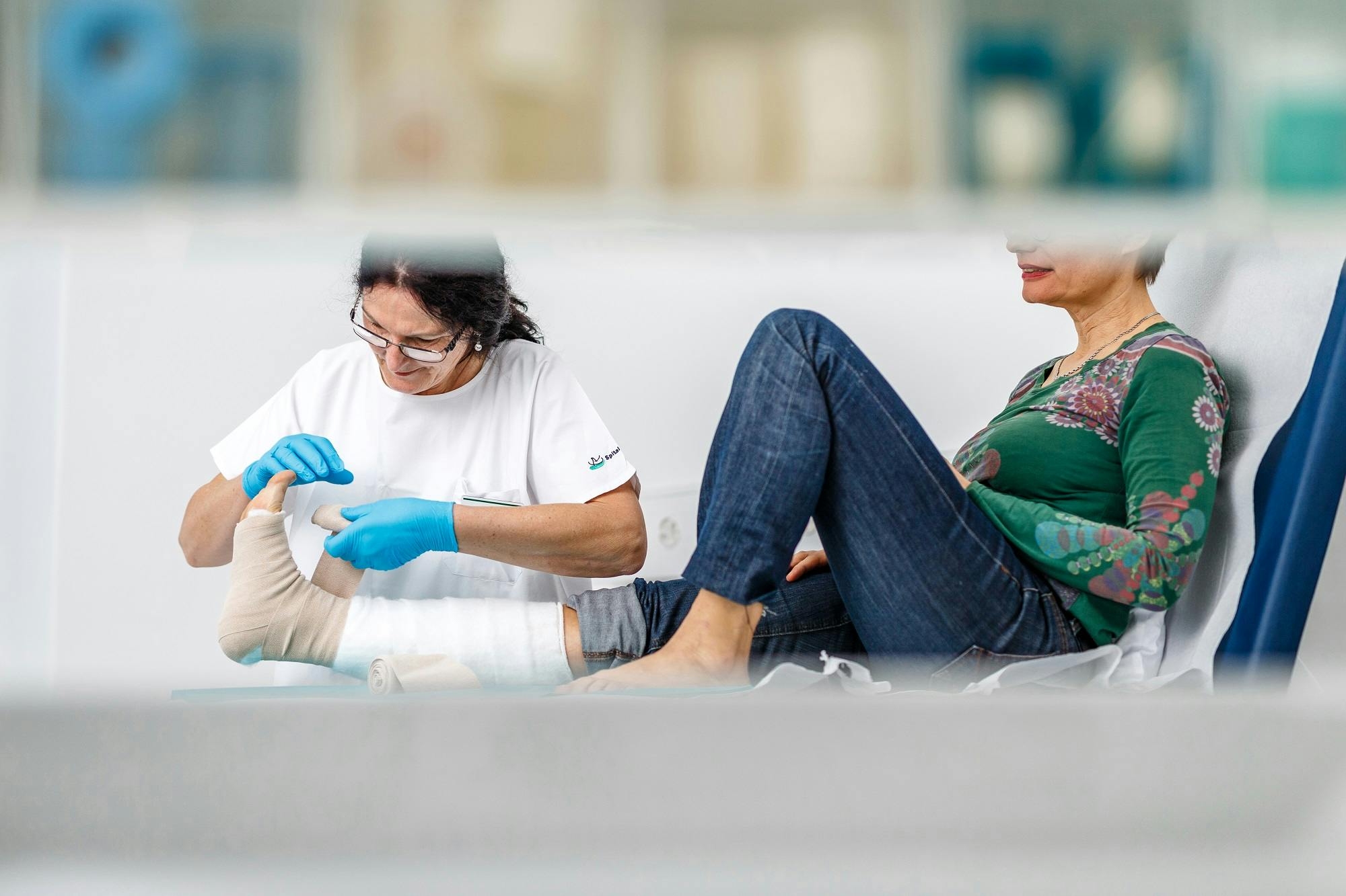 Zwei Personen sitzen auf dem Boden, wobei die eine Person der anderen eine Fußpflege gibt.