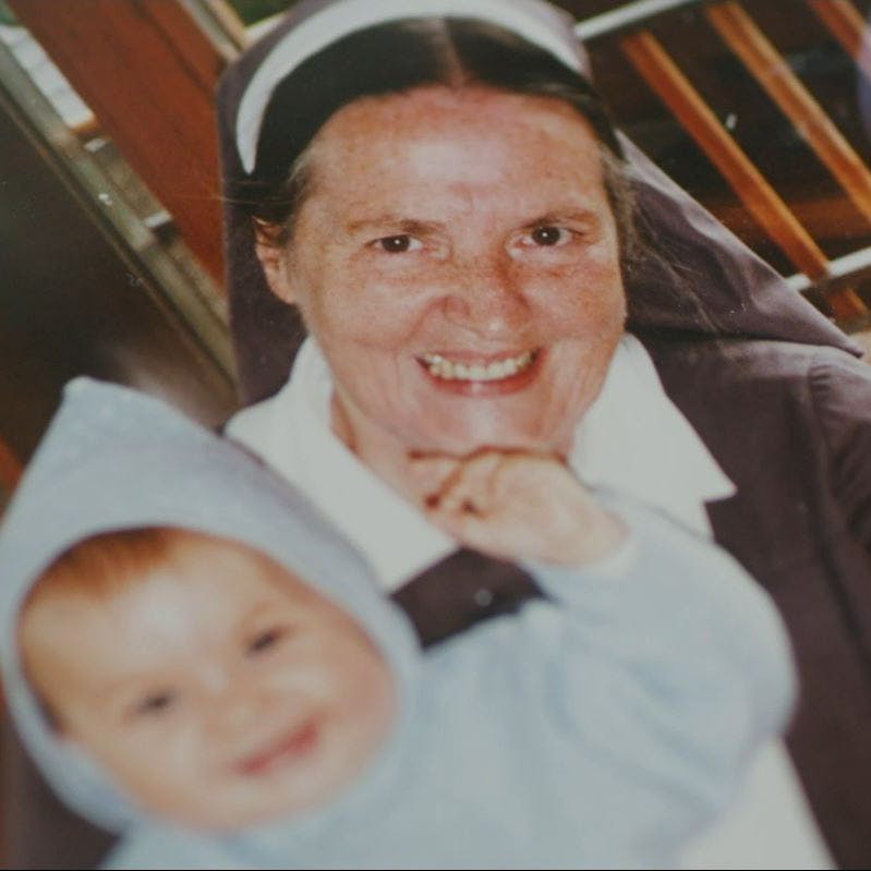 Lächelnde Nonne mit Kleinkind in Haube.